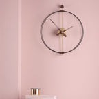 Modern wall clock with black frame and gold accents on a pink wall.