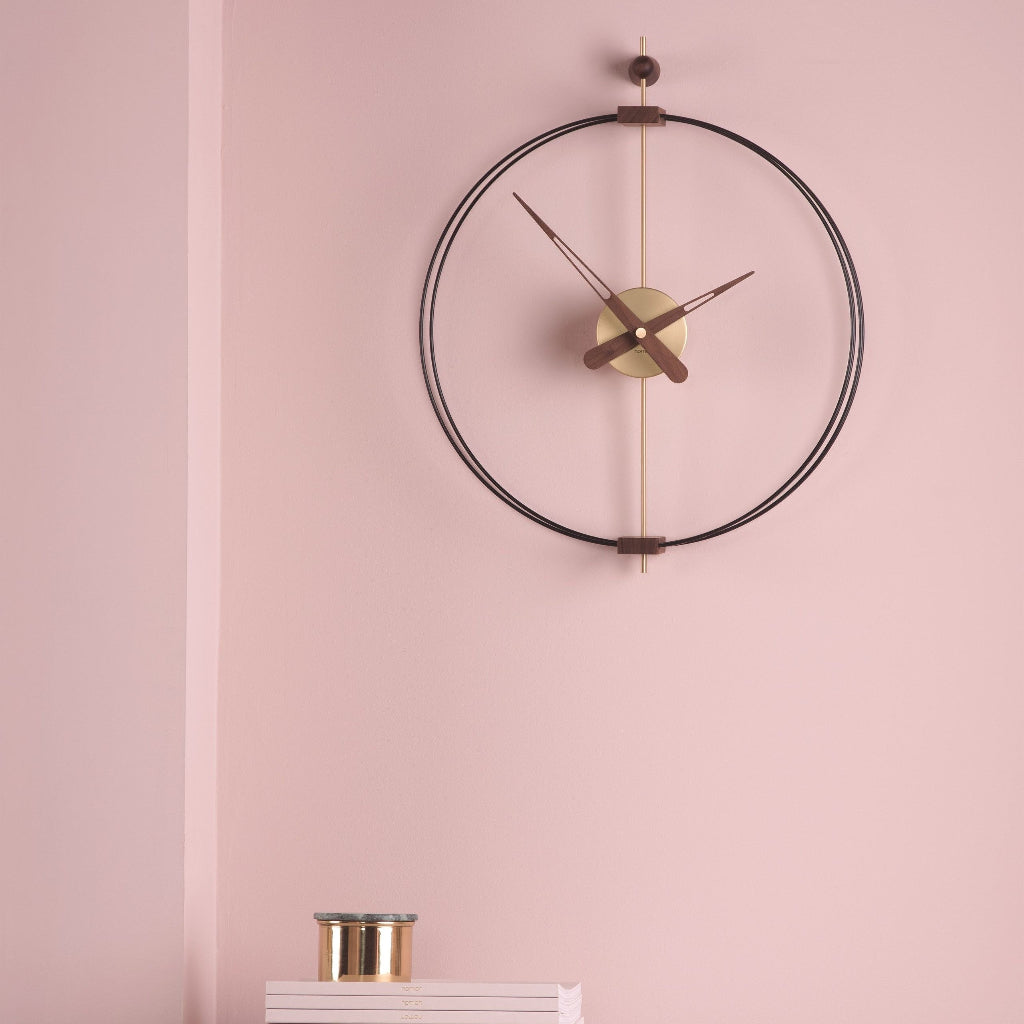 Modern wall clock with black frame and gold accents on a pink wall.