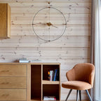Wooden cabinet with books and a chair against a wooden wall with a round clock.