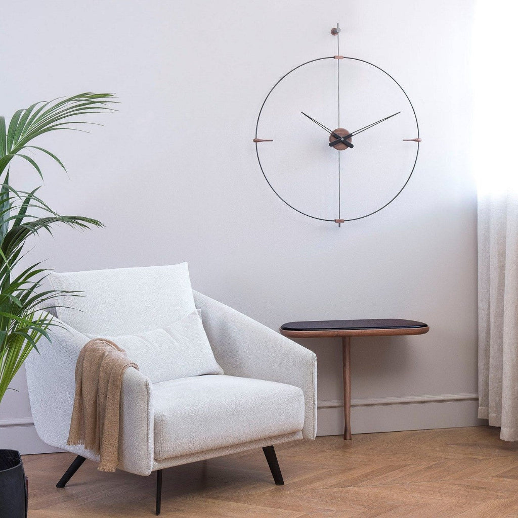 White armchair with a blanket, wooden side table, and decorative wall clock in a room.
