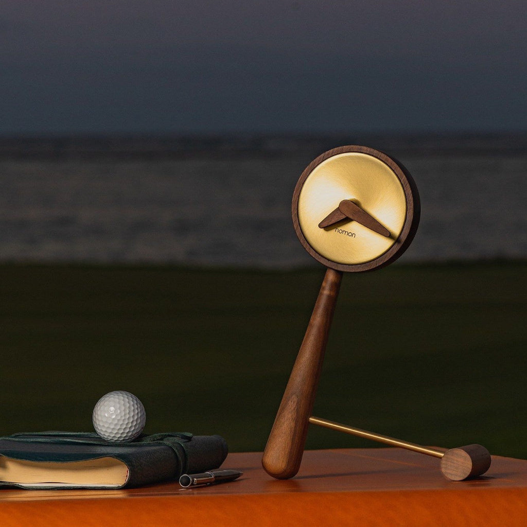 Decorative clock with golf-themed design on a wooden surface with a blurred background