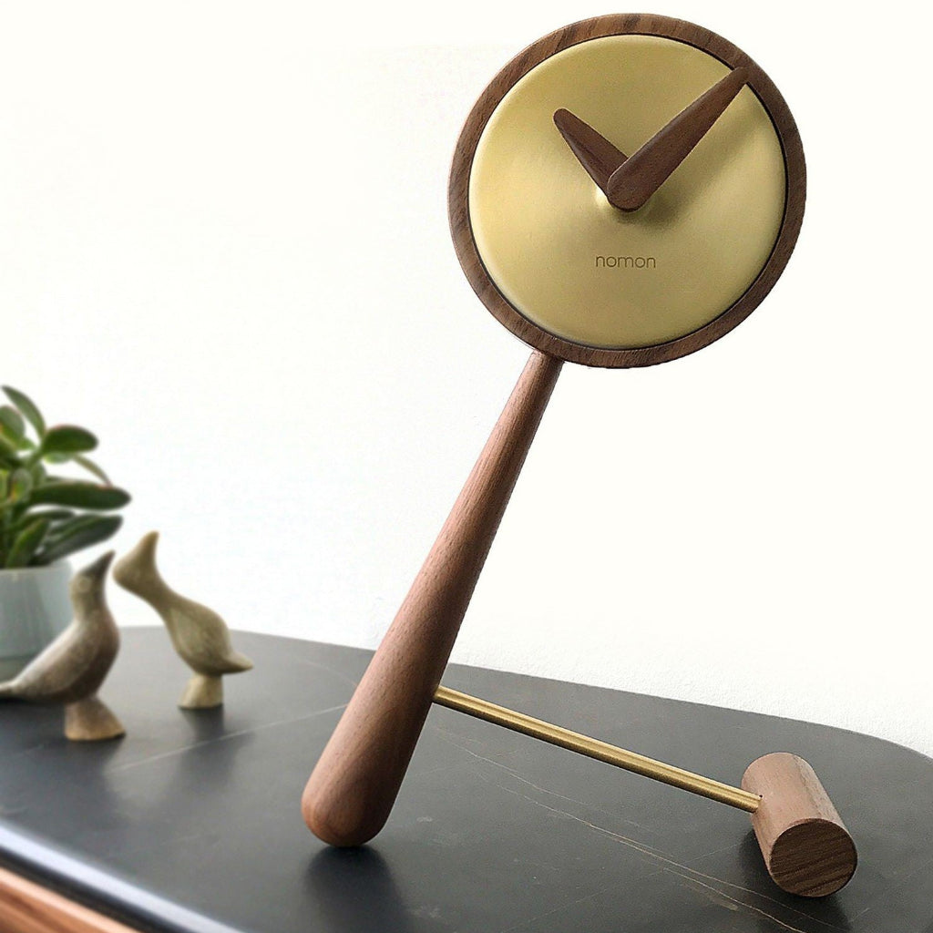 Wooden clock with a yellow face on a dark surface, featuring the brand 'Nomon'.