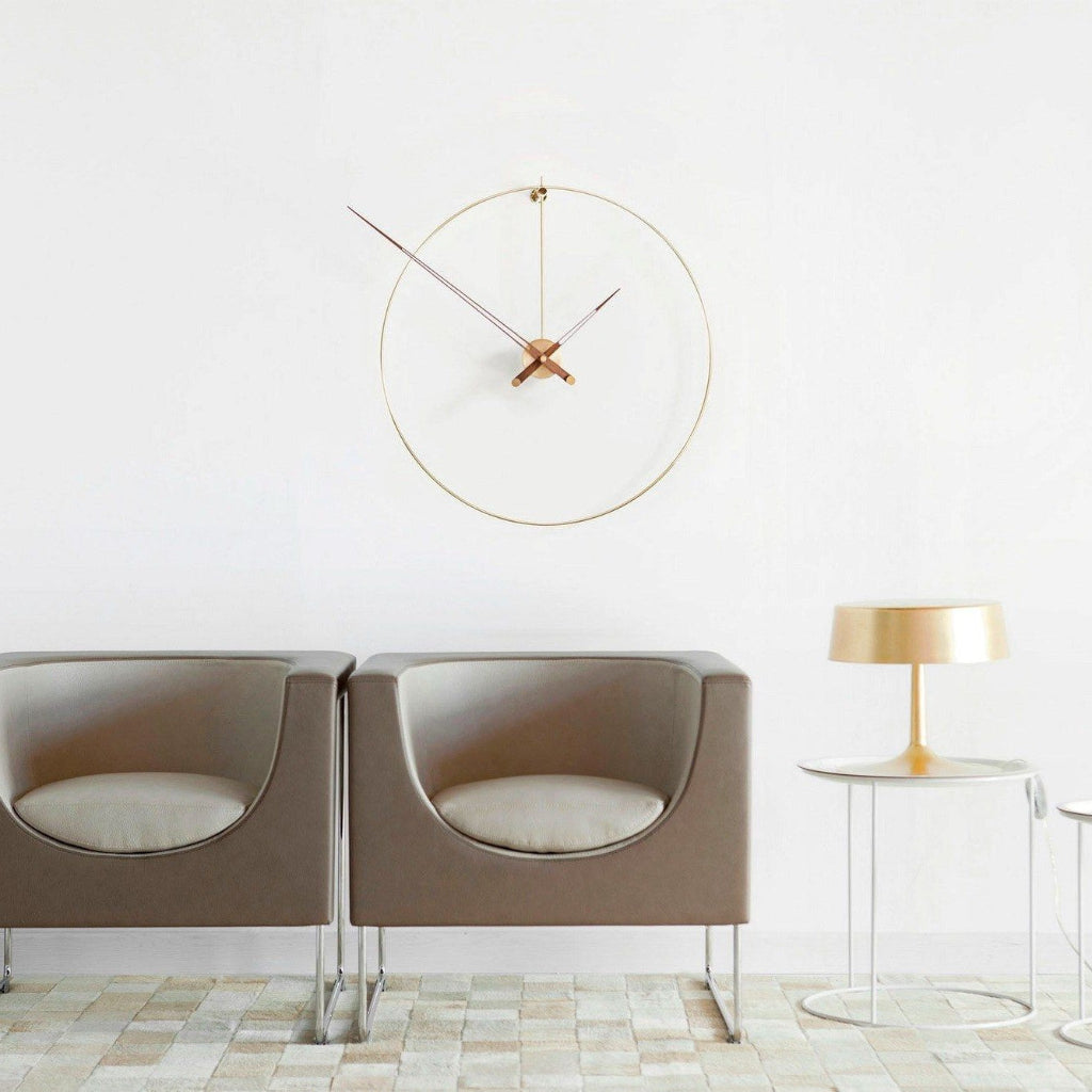 Modern interior with two beige chairs, a round gold clock, and a small table with a lamp.