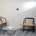 Modern interior with wooden chairs and a glass coffee table against a white wall with a clock.