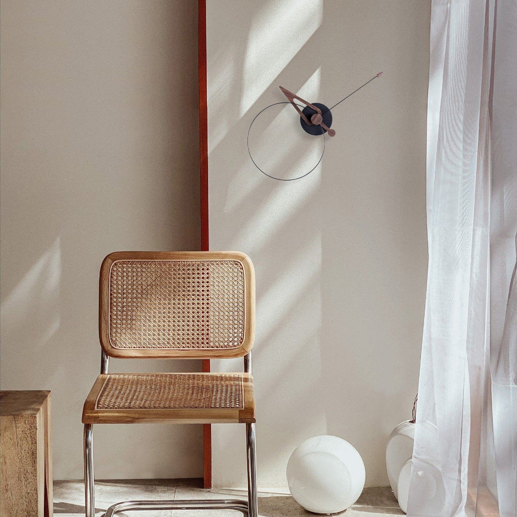 Wicker chair in a room with a clock on the wall and a curtain.