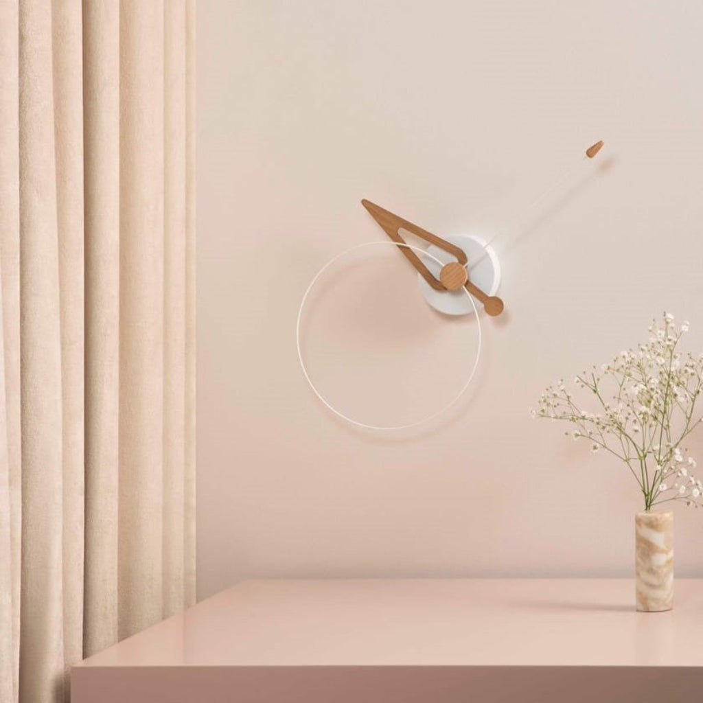 Minimalist wall clock on a light pink wall with a vase of flowers on a matching surface.