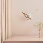 Minimalist wall clock on a light pink wall with a vase of flowers on a matching surface.