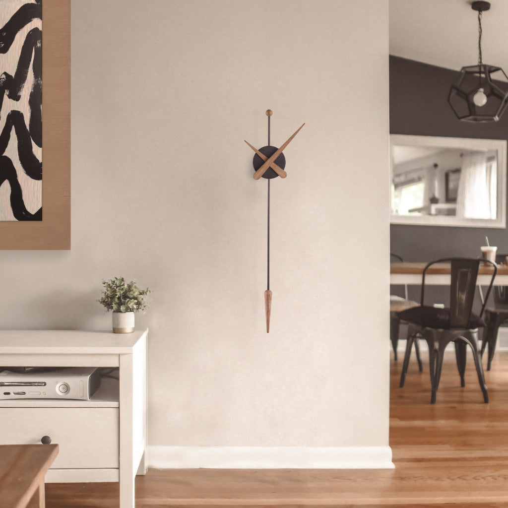 Modern wall clock on a neutral wall with a view of a dining area in the background.