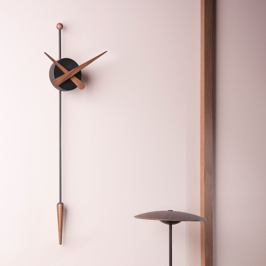 Modern wall clock with long pendulum on a light pink wall