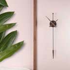 Modern wall clock with long thin design on a light pink background with green leaves.