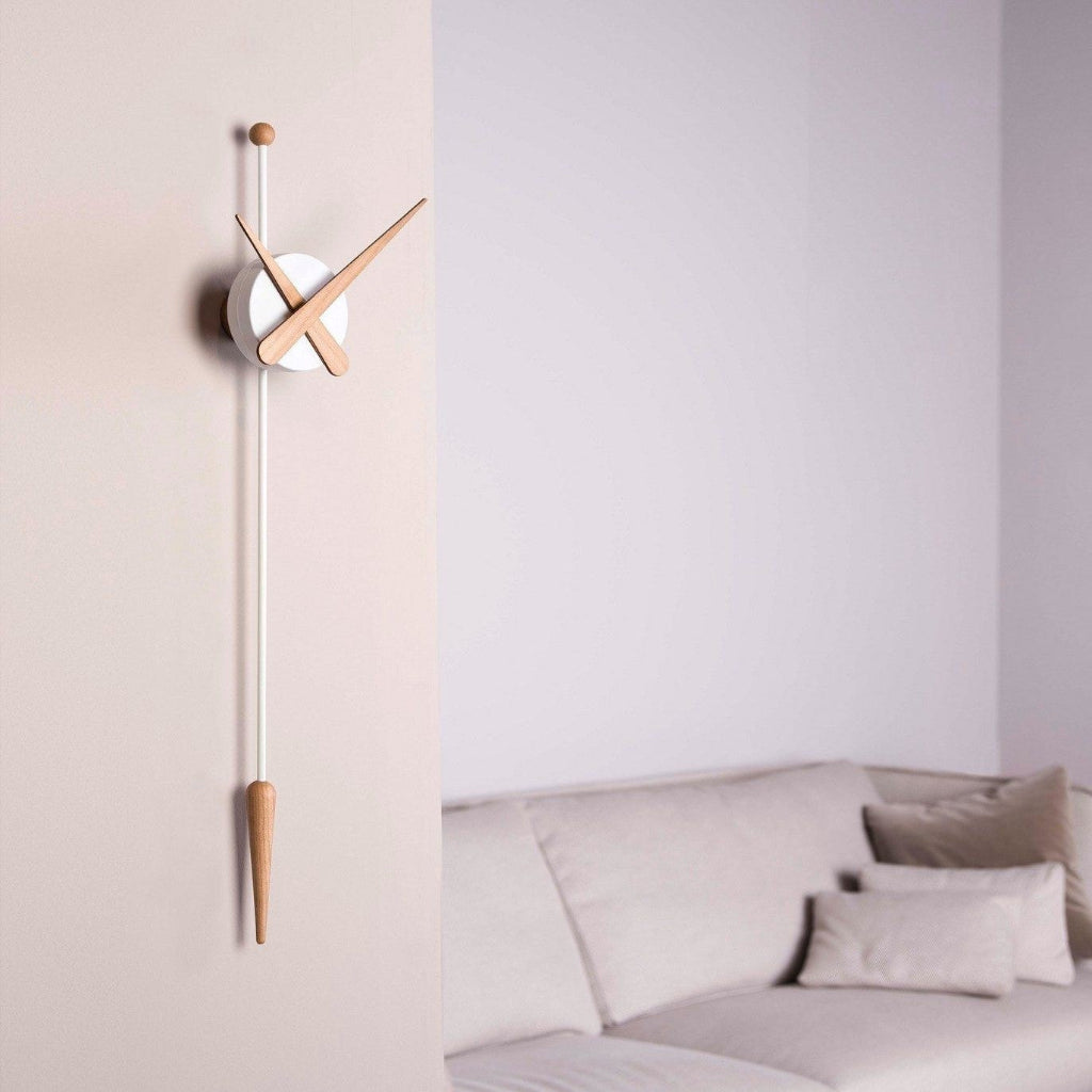Modern wall clock with long thin design on a light-colored wall above a sofa.