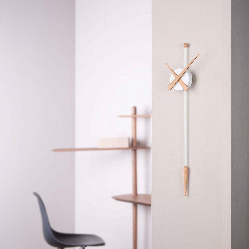 Modern wall clock with wooden accents on a gray wall with a chair and shelf in the background.
