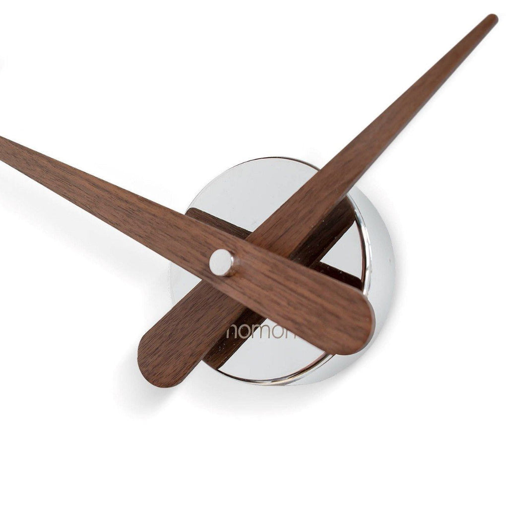 Wooden clock hands on a white background with 'nomad' branding.