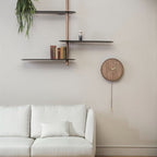 Wooden wall clock on a beige wall with shelves and a white sofa.