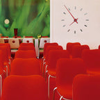 Nomon Spain Tacon L 12 Red on a white wall behind red chairs of auditorium available at Spacio India for luxury home decor collection of Timepieces & Clocks.