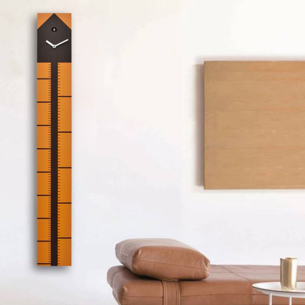 Wall clock with ruler design on a white wall above a brown sofa.