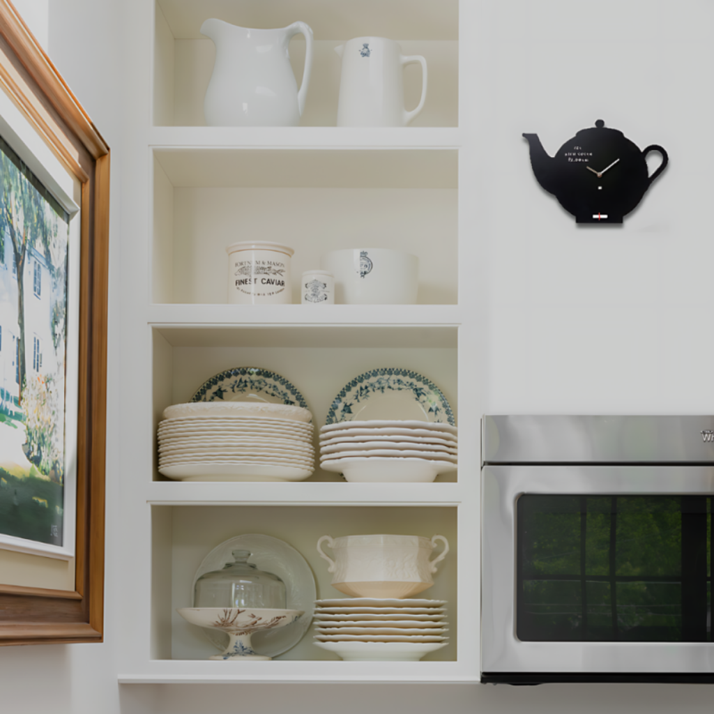 Kitchen interior with white shelves displaying dishes, a black teapot-shaped clock, and a stainless steel oven.