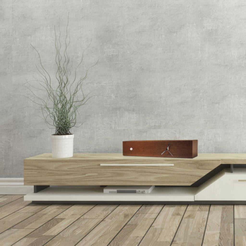 Modern wooden TV stand with a plant and decorative box against a gray wall.