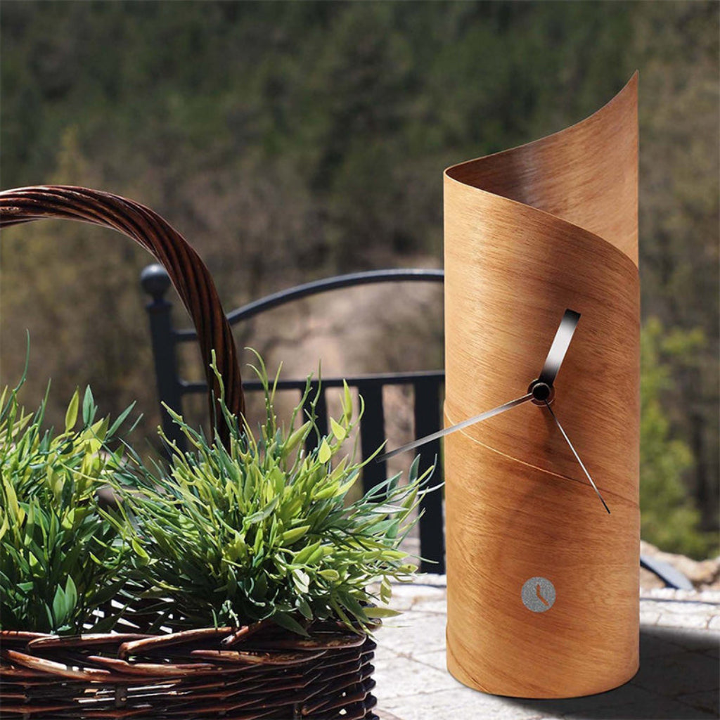 Wooden clock with wavy design outdoors next to a basket of plants from Tothora available at Spacio retail stores in Mumbaii & Kolkata and online.